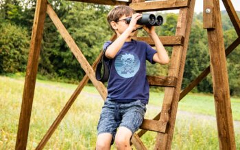 Bub schaut durch ein Fernglas am Hochstuhl