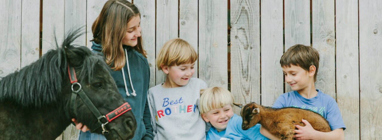 4 Kinder stehen am Stall neben einem Pony und halten ein Zieglein