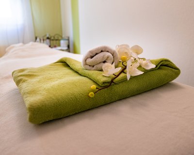 Massageliege mit grünem Handtuch, weißem Handtuch und weißer Orchidee darauf