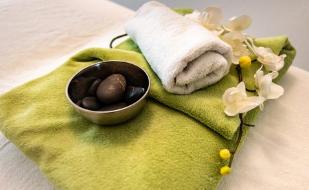 Gefaltetes grünes Handtuch mit weißem Handtuch, Schale mit schwarzen Steinen und weißen Orchideen auf hellem Untergrund