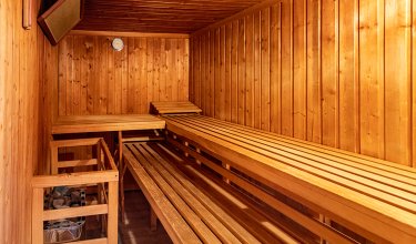 Innenansicht einer Holzsauna mit Bänken, Ofen und Thermometer an der Wand