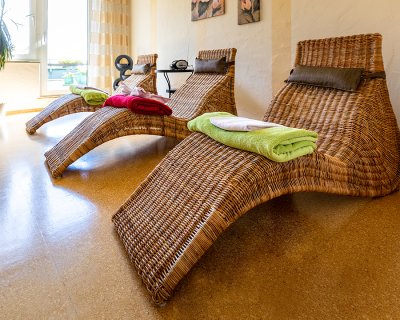 Drei geflochtene Liegen mit bunten Handtüchern in einem hellen Raum mit Pflanzen und Bildern an der Wand