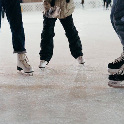 Drei Personen mit Schlittschuhen auf einer Eisbahn, Nahaufnahme der Beine und Füße