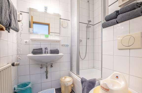 Kleines Badezimmer mit Waschbecken, Spiegel, Dusche und Handtüchern auf Regalen
