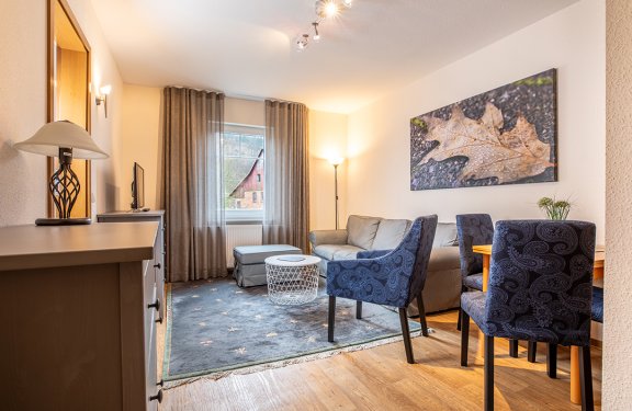 Wohnzimmer mit grauem Sofa, blau gemusterten Stühlen, Teppich und großem Blattbild an der Wand