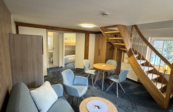 Wohnzimmer mit blauem Sofa, Sesseln, Holztisch, Treppe und Blick in angrenzende Zimmer