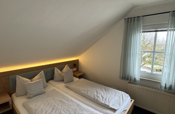 Schlafzimmer mit zwei Einzelbetten unter schräger Decke neben Fenster mit Vorhängen