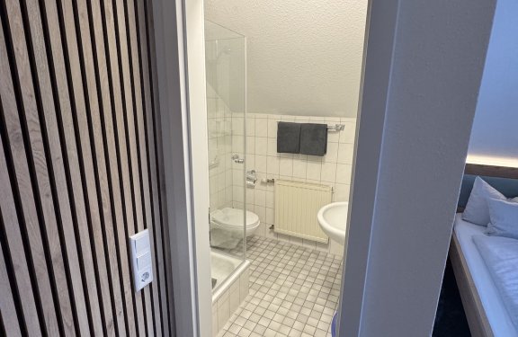 Blick durch Tür auf kleines Badezimmer mit Dusche, Toilette, Waschbecken und Handtüchern