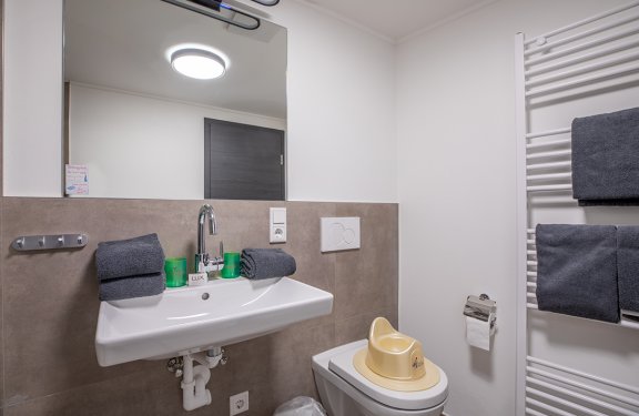 Badezimmer mit Waschbecken, Spiegel, Handtüchern, WC mit Kindertoilette und Handtuchheizung