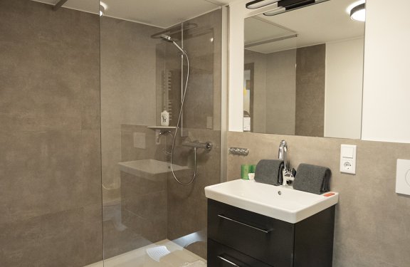 Modernes Badezimmer mit begehbarer Dusche links, Waschbecken mit Spiegel und Handtüchern rechts