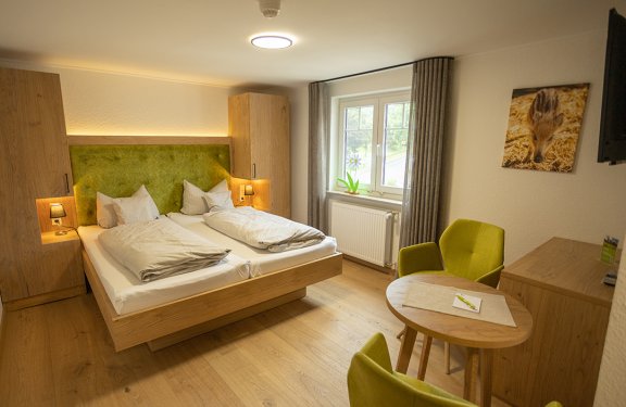 Helles Hotelzimmer mit Doppelbett, grüner Polsterung, zwei grünen Sesseln und Fenster mit Vorhängen