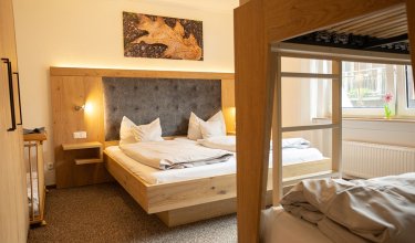Gemütliches Schlafzimmer mit Doppelbett, Etagenbett rechts und herbstlichem Blattbild an der Wand
