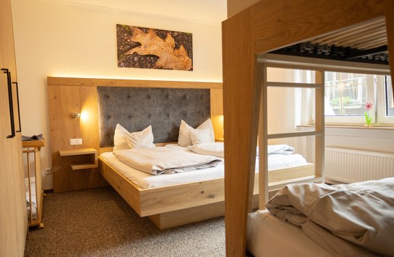 Gemütliches Schlafzimmer mit Doppelbett, Etagenbett rechts und herbstlichem Blattbild an der Wand