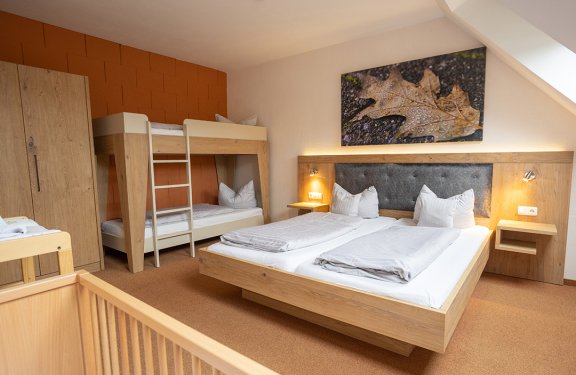 Zimmer mit Doppelbett, Etagenbett, Babybett und herbstlichem Blattbild an der Wand
