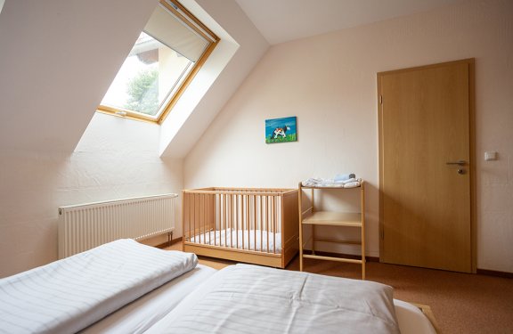 Schlafzimmer mit Dachfenster, Babybett und Wickeltisch neben Holztür