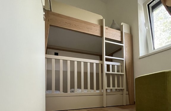 Kinderzimmer mit Etagenbett aus Holz neben einem Fenster und grünem Sitzmöbel