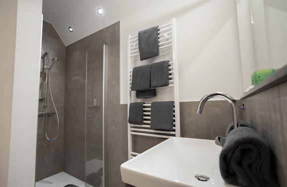 Modernes Badezimmer mit Dusche, Handtüchern an Heizkörper und Waschbecken mit Wasserhahn