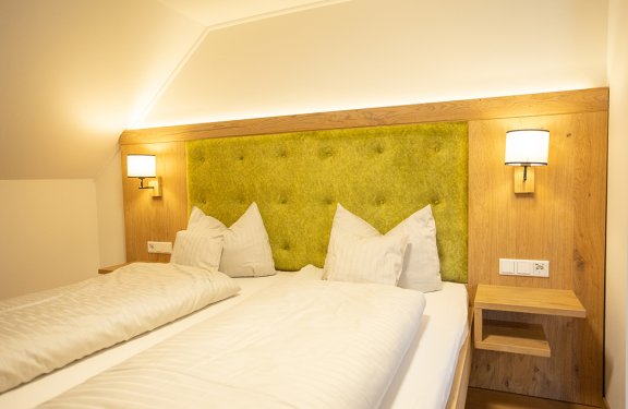 Hell beleuchtetes Schlafzimmer mit grünem gepolstertem Kopfteil und zwei Einzelbetten