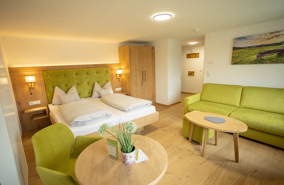 Helles Hotelzimmer mit Doppelbett, grünem Sofa, Tisch mit Stühlen und Holzboden