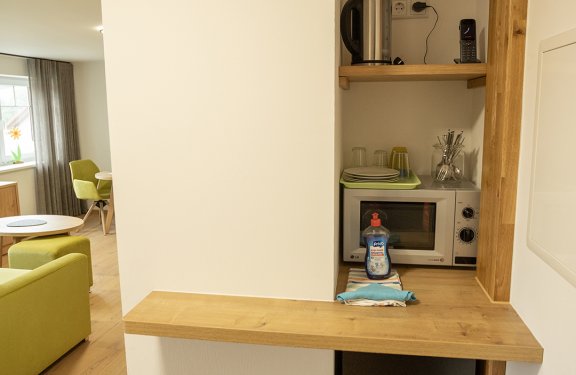 Kleine Küchenzeile mit Mikrowelle, Wasserkocher, Geschirr und Spülmittel neben einem Holzthekenbrett