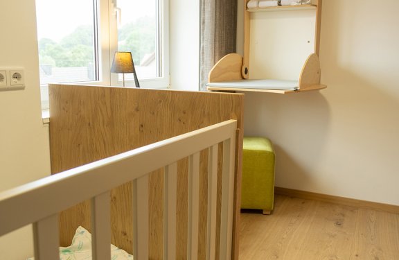 Kinderzimmer mit Holzgitterbett links, Fenster und Wandwickeltisch mit gelbem Deckel rechts
