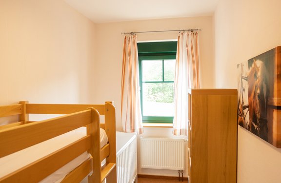 Schmales Schlafzimmer mit Etagenbett, Kinderbett, Fenster mit Vorhängen und Holzschrank