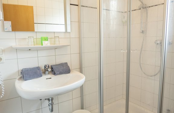 Kleines Badezimmer mit Dusche, Waschbecken, Spiegel und Handtüchern auf dem Waschbecken