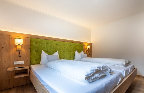 Modernes Schlafzimmer mit Doppelbett, grünem gepolstertem Kopfteil und zwei Wandlampen