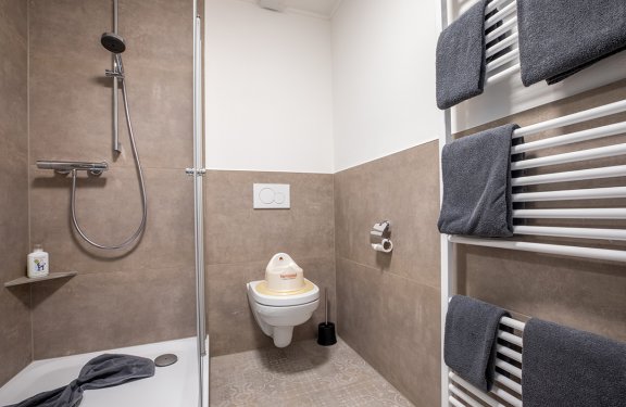 Modernes Badezimmer mit Dusche links, Toilette mit Kindersitz in der Mitte und Handtüchern rechts am Heizkörper