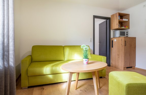 Grünes Sofa und Hocker vor rundem Holztisch mit Blumentopf in hellem Wohnzimmer