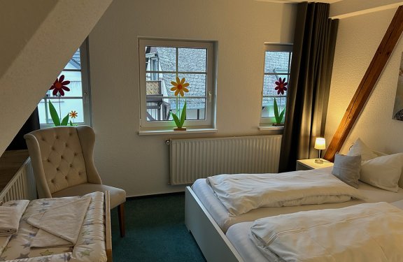Gemütliches Schlafzimmer mit zwei Betten, Sessel links, Fenster mit Blumenaufklebern und Nachttischlampe rechts