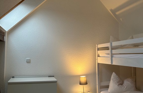 Schlafzimmer mit Etagenbett rechts, Nachttisch mit Lampe und Kommode links unter Dachschräge