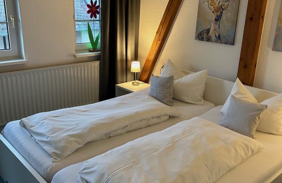 Hell eingerichtetes Schlafzimmer mit zwei Betten, Nachttischlampe und Hirschbild an der Wand