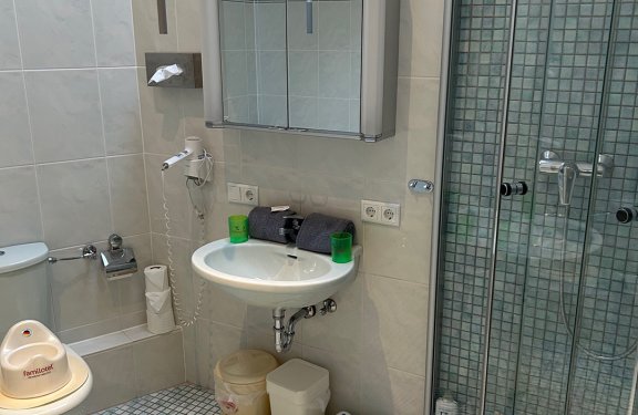 Kleines Badezimmer mit Toilette, Waschbecken, Spiegel, Duschkabine und Kindersitz auf der Toilette