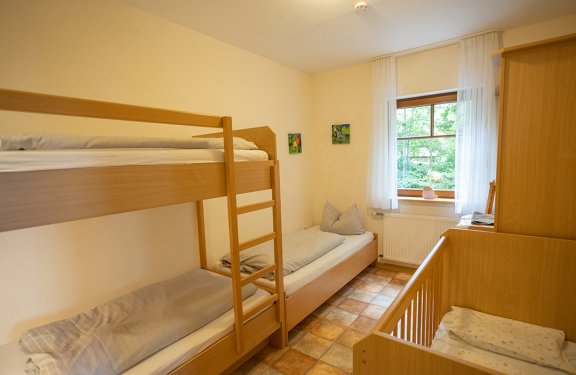 Kleines Schlafzimmer mit Etagenbett, Einzelbett und Babybett neben Fenster mit weißen Vorhängen