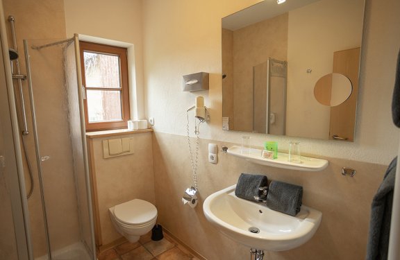 Kleines Badezimmer mit Dusche links, Toilette unter Fenster und Waschbecken mit Spiegel rechts