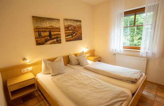 Hell eingerichtetes Schlafzimmer mit zwei Einzelbetten, Holzmöbeln und Fenster mit Blick ins Grüne