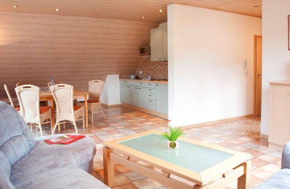 Helles Wohnzimmer mit grauem Sofa, Holztisch mit Pflanze und Essbereich neben offener Küche