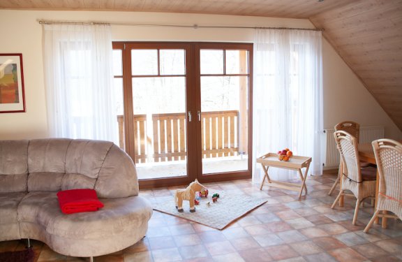 Helles Wohnzimmer mit grauem Sofa, Spielzeug auf Teppich vor Glastür zum Balkon, Esstisch mit Stühlen