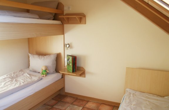 Kinderzimmer mit Etagenbett, Kuschelpuppe auf unterem Bett und Bücherregal an der Wand