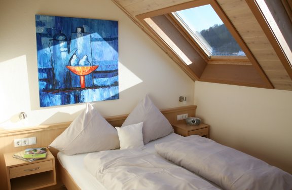Hell beleuchtetes Schlafzimmer mit Dachfenster, Doppelbett und blauem Gemälde an der Wand