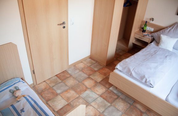 Blick auf ein Zimmer mit zwei Betten, einem Nachttisch mit Weinflasche und Gläsern, und einem offenen Schrank