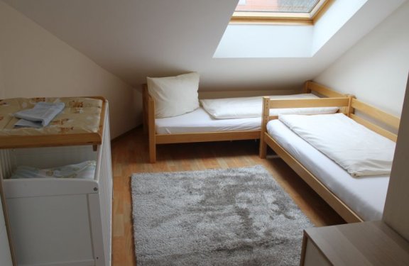 Kleines Schlafzimmer mit zwei Einzelbetten unter einem Dachfenster und einem Wickeltisch links