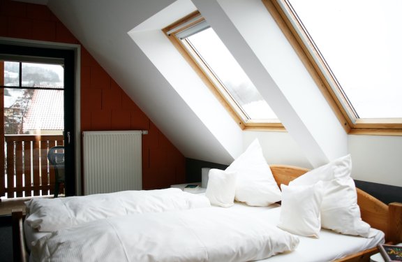 Hell eingerichtetes Schlafzimmer mit Dachfenstern, weißer Bettwäsche und Balkon mit Blick nach draußen