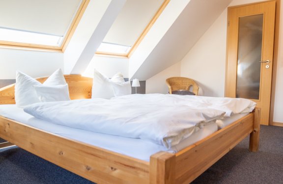 Helles Schlafzimmer mit Holzbett unter Dachschrägen und zwei Fensterrollos