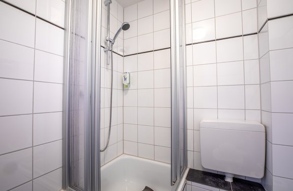 Kleine Duschkabine mit weißen Fliesen, Duschkopf und Seifenspender an der Wand