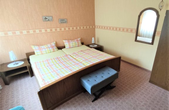 Schlafzimmer mit Doppelbett, karierten Bettdecken, zwei Nachttischen mit Lampen und Spiegel an der Wand