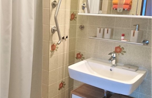 Helles Badezimmer mit Waschbecken, Spiegel, Handtüchern und Duschvorhang links