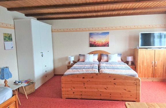 Schlafzimmer mit Holzbett, weißen Schränken, Fernseher und blauer Lampe auf rotem Teppichboden