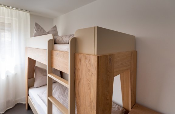 Moderner Etagenbett aus Holz mit beigen Kissen und Tageslicht durch Fenster mit Vorhang